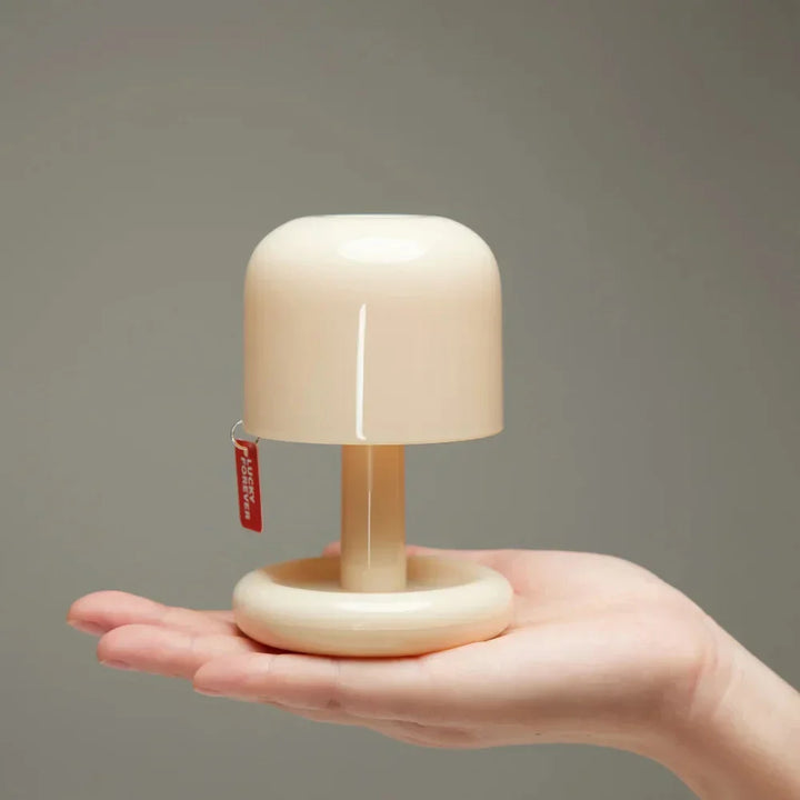 Miniature table lamp with a cream-colored dome shade resting on an open palm.