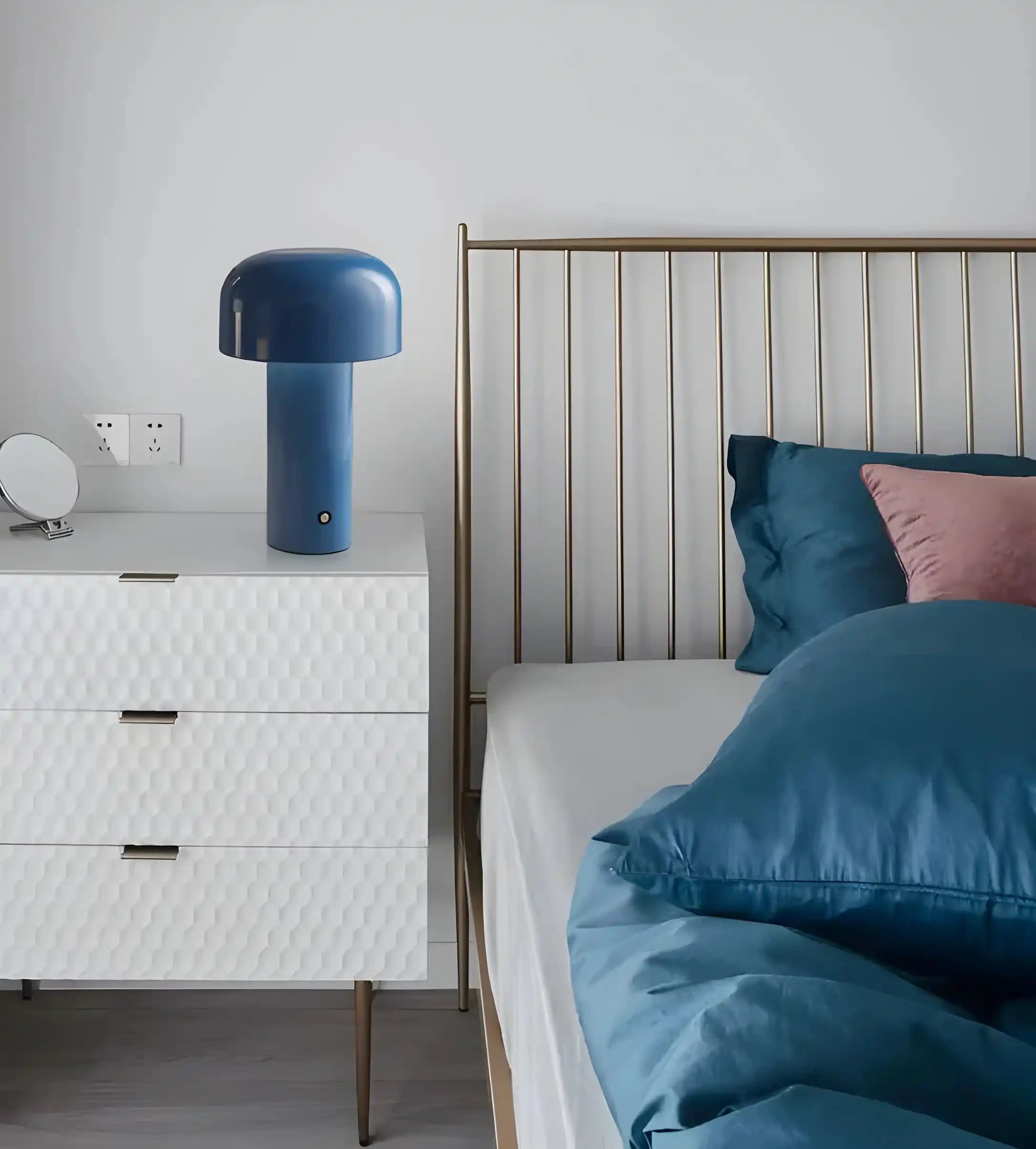 Modern bedroom featuring a metal-framed bed with blue bedding and a white dresser topped by a blue mushroom-shaped lamp.