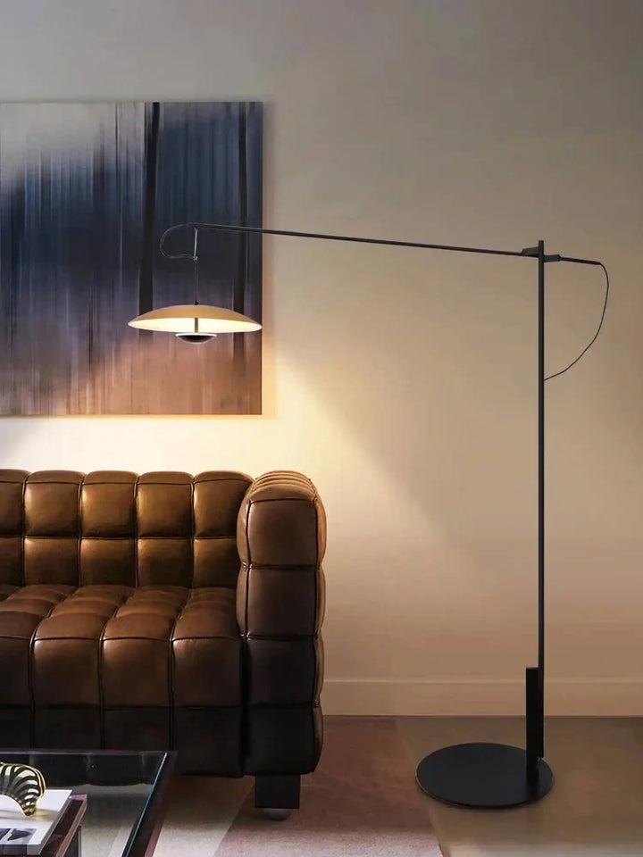 Sleek floor lamp with an adjustable arm and disc-shaped shade illuminating a leather sofa.