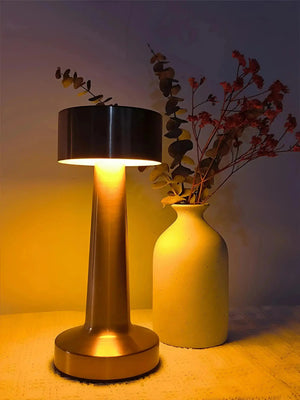 Table lamp with a cylindrical base and black drum shade emitting warm light.